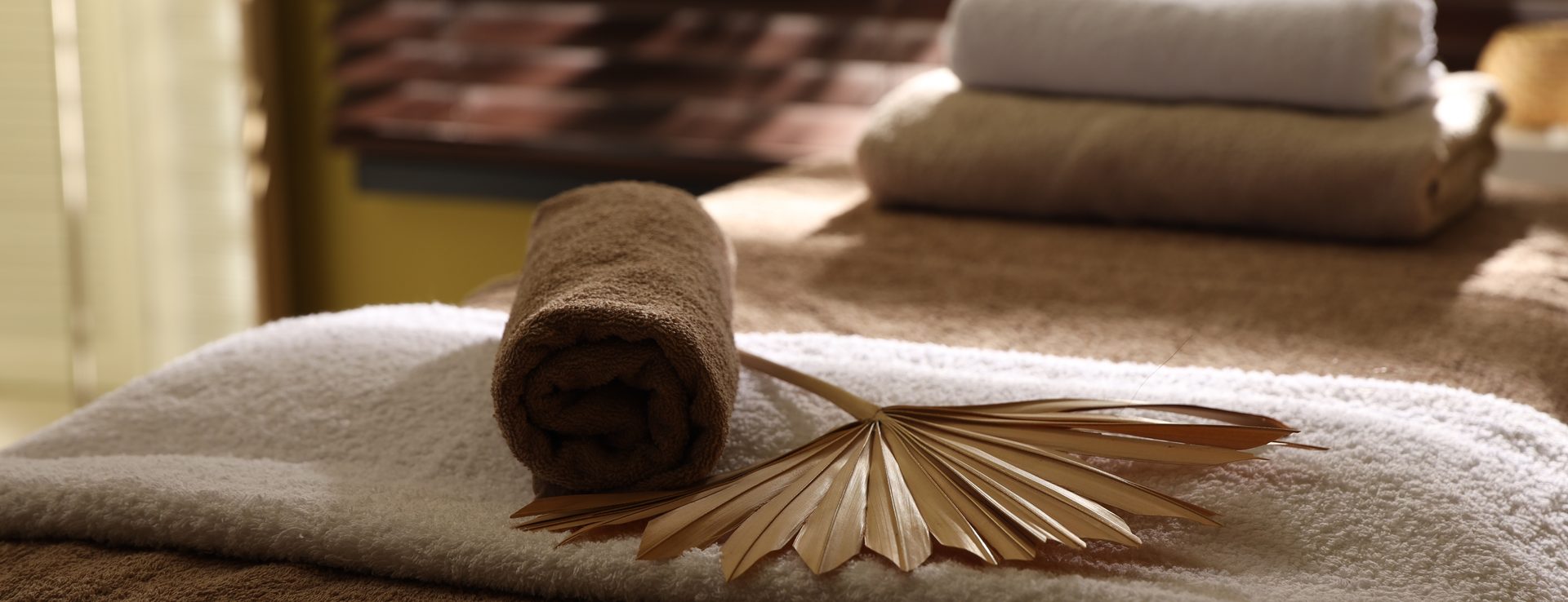 Table de massage avec serviettes roulées et feuille de palmier