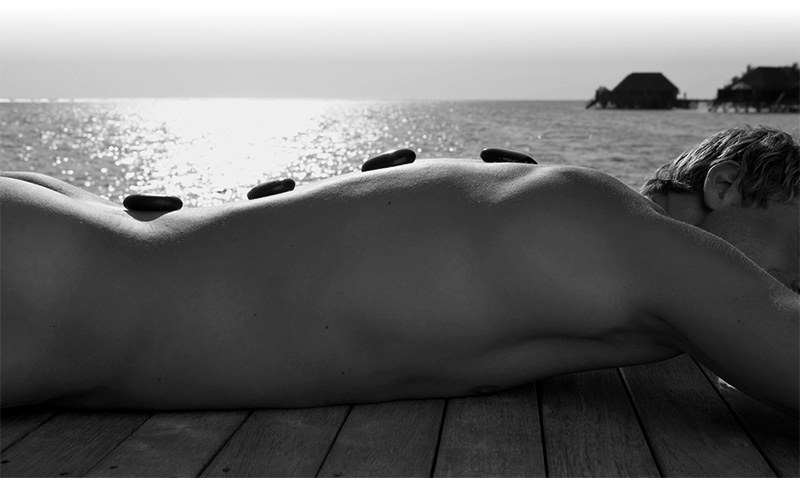 Homme allongé face à la mer, galets chauds sur le dos, photo noir et blanc
